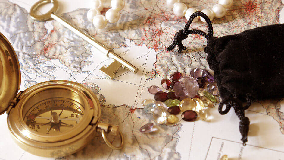 Der mögliche Schatz einer Schnitzeljagd: Eine Landkarte mit einem Kompass, einer Perlenkette, einem Beutel mit bunten Steinen und einem Schlüssel darauf liegend.