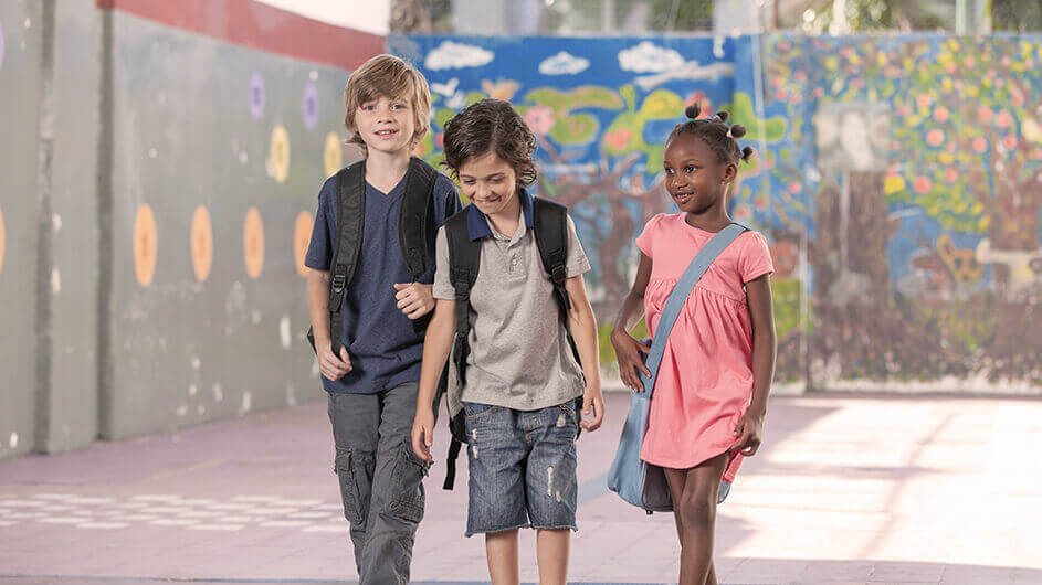zwei Jungen und ein Mädchen gehen über den Schulhof und lächeln dabei