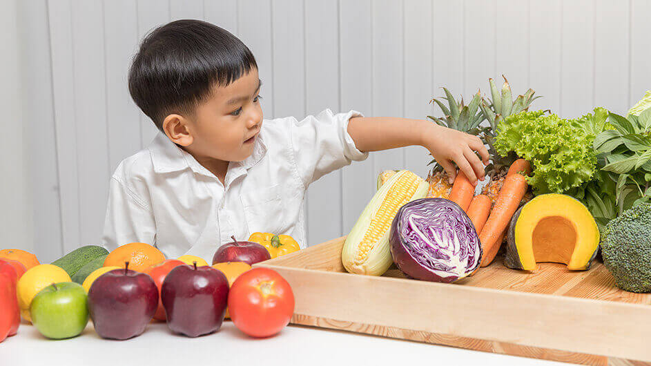 Ein Kind sucht sich aus verschiedenem Gemüse und Obst eine Möhre aus.