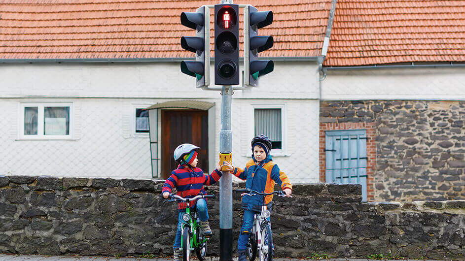 zwei kleine Schuljungen mit Fahrradhelmen sitzen auf Fahrrädern und warten an der roten Ampel auf Grün