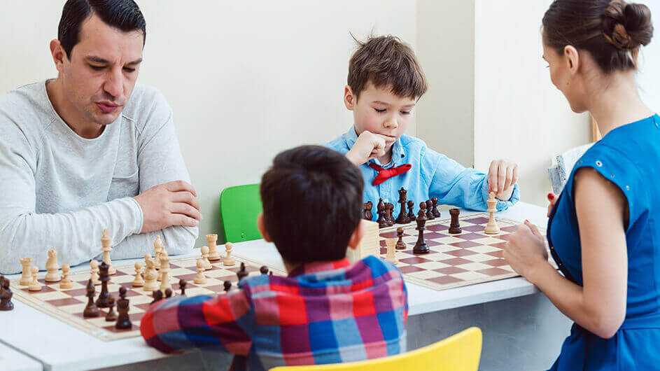 Eine Familie mit zwei Kindern beim Schachspielen. Alle gucken konzentriert auf die Schachbretter.
