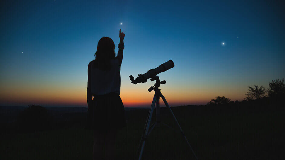 Die Silhouette eines Mädchens mit Teleskop vor dem Nachthimmel. Das Kind zeigt auf einen Stern.