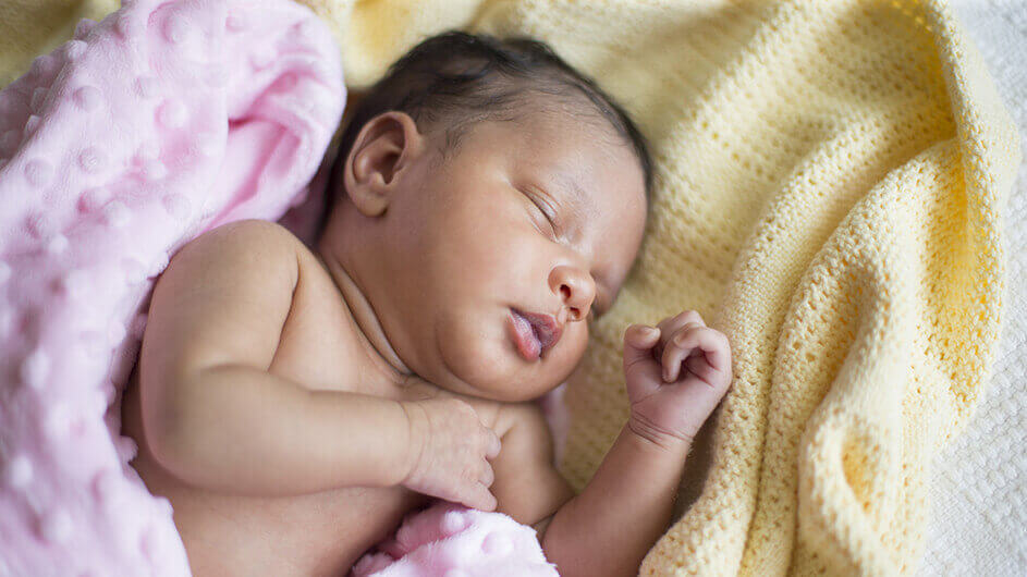 Ein schlafendes Baby (ein Neugeborenes) zwischen kuscheligen Decken.