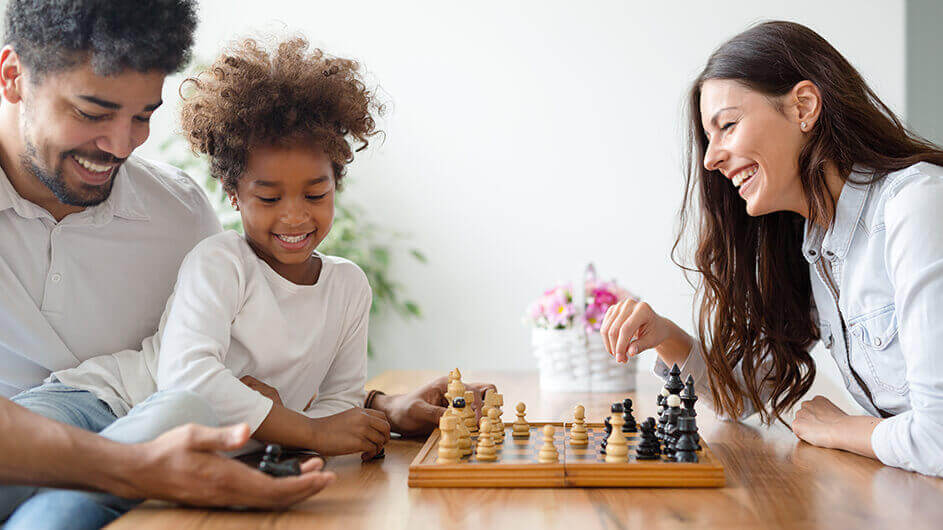 Eine glückliche Familie (Kind, Mutter und Vater) beim Schachspielen. Sie lächeln.