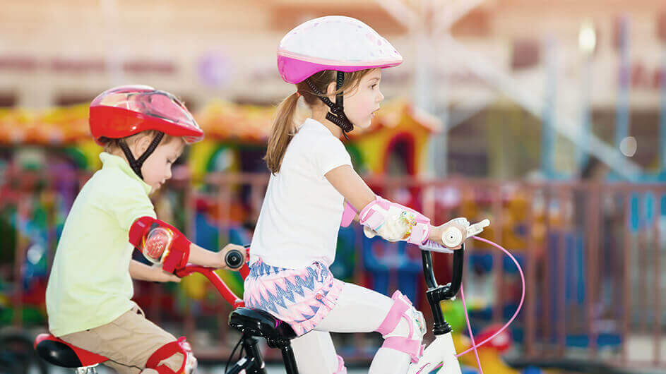 In der Seitenansicht: Zwei kleine Kinder fahren mit Helmen und Schützern geradeaus nebeneinander Fahrrad.