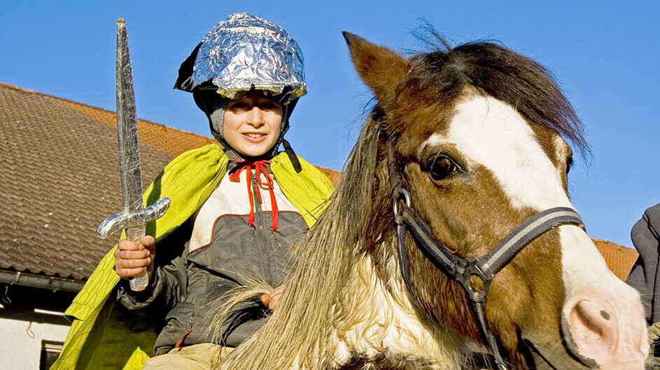 Junge verkleidet als der heilige sankt martin von Tours auf einem Pferd mit Helm, Schwert und Mantel bei Sonnenschein