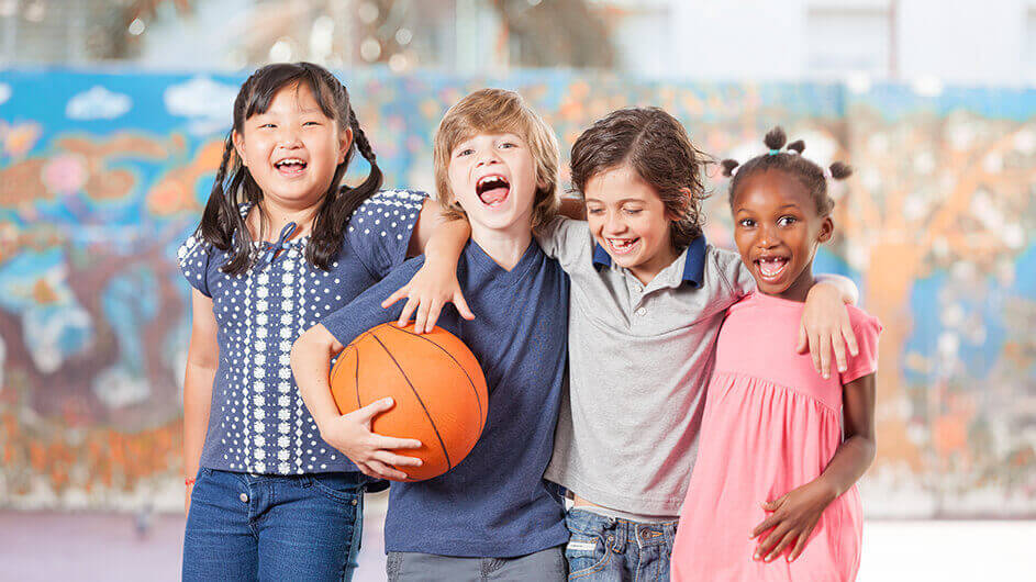 Vier Kinder mit einem Basketball: Die Kids lachen und umarmen sich.