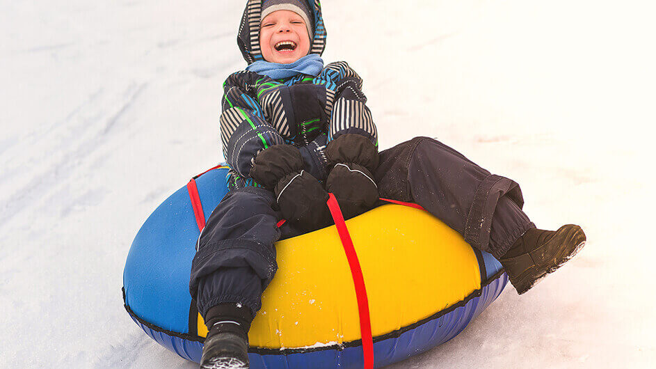 Ein fröhlicher Junge beim Rodeln auf Schneereifen