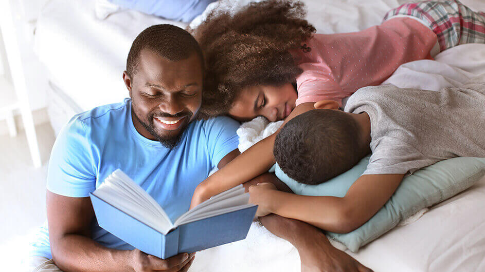 Ein lächelnder Vater liest seinen beiden Kindern eine Gutenachtgeschichte vor
