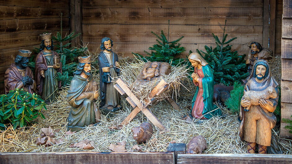 Eine Weihnachtskrippe mit Holzfiguren, Stroh und kleinen Tannenbäumen auf einem Weihnachtsmarkt