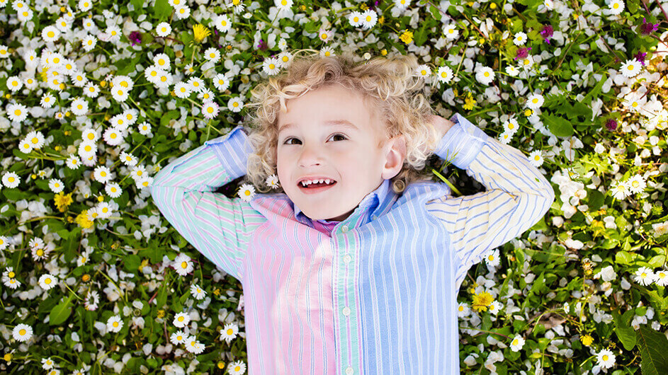 Ein Junge liegt lächelnd träumend auf einer Blumenwiese mit Löwenzahn und Gänseblümchen