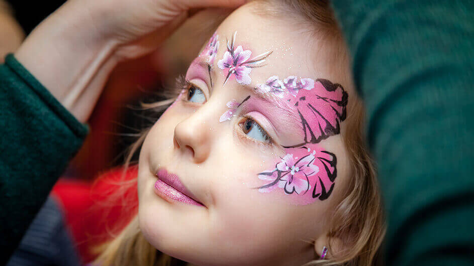 Kind wird geschminkt als Fee mit einem rosa Shcmetterlink-Ornament
