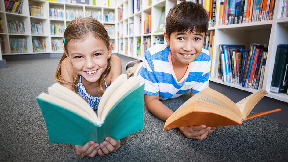 Lachende Kinder liegen lesend mit Büchern auf dem Boden einer Bibliothek