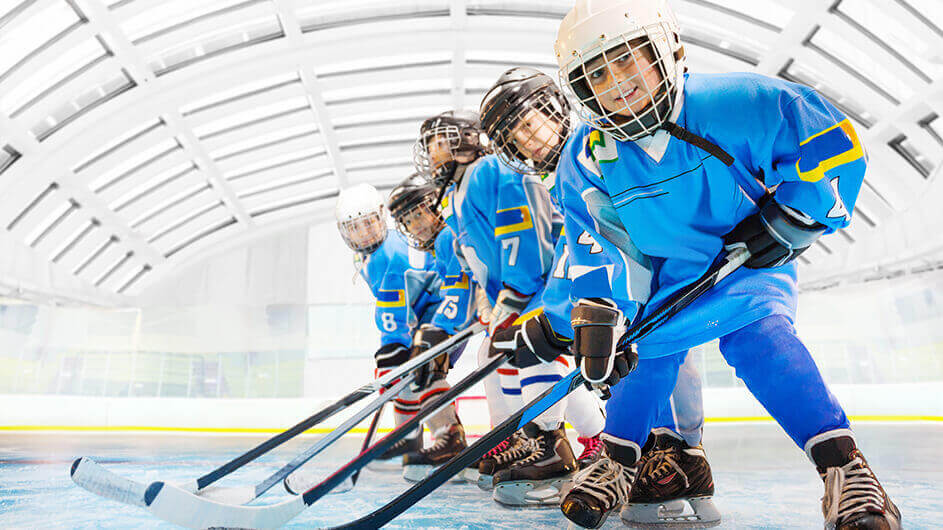 Lächelnde Kinder in Schutzkleidung mit Schlägern beim Spielen von Eishockey