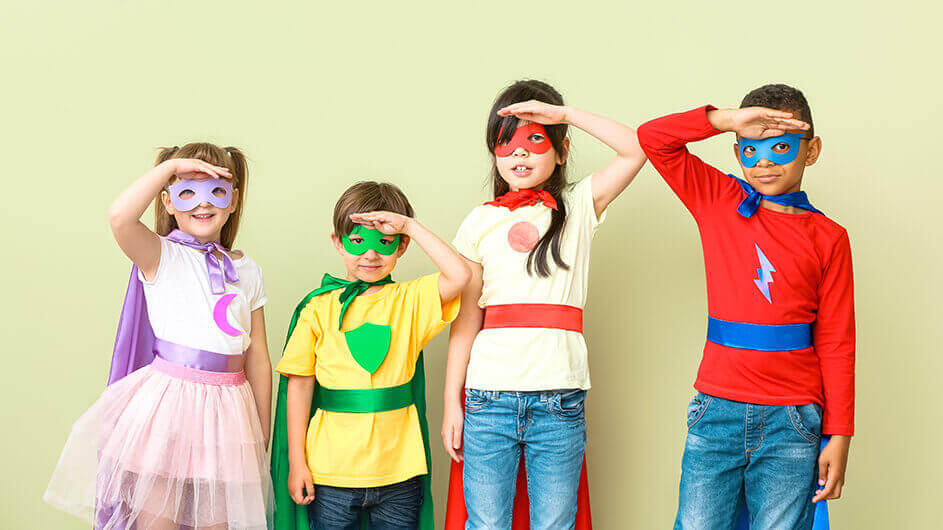 Kinder verkleidet als Superheldinnen und Superhelden: Sie halten die Hände in die Ferne guckend über die Stirn. Sie tragen bunte Masken und Capes.