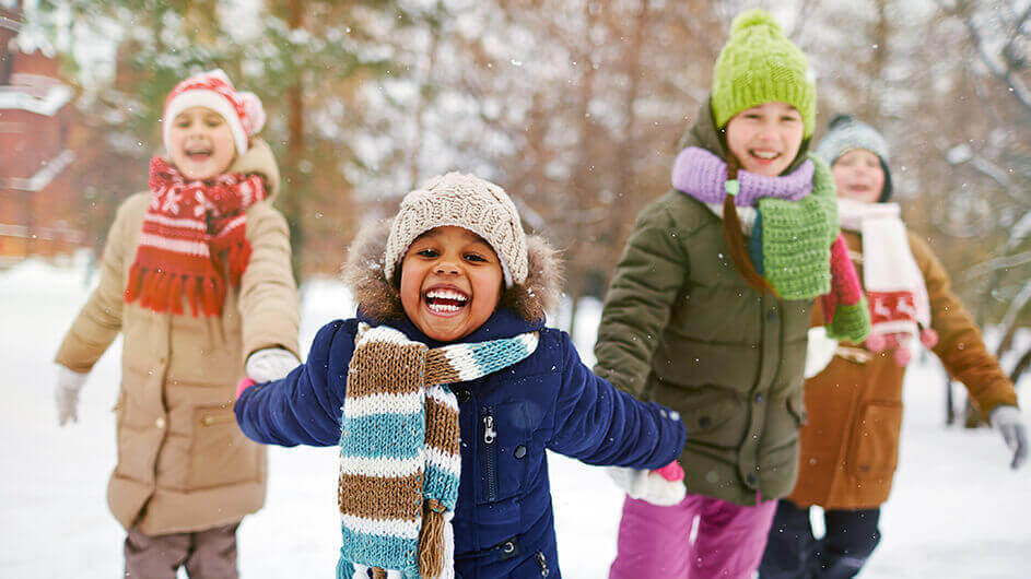 Fröhliche Kinder laufen Händchen halten durch den Schnee im Feriencamp
