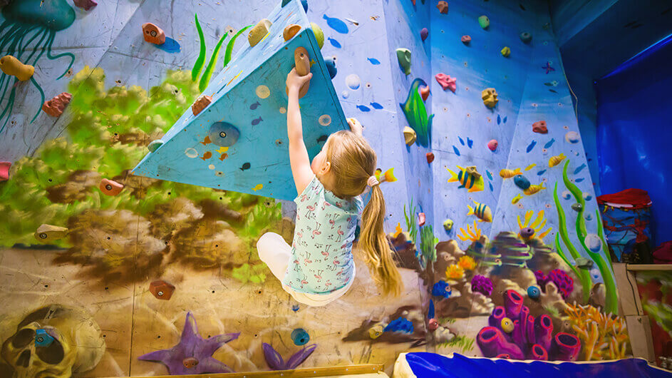 Ein kleines Mädchen beim Bouldern an einer Kletterwand in einer Boulderhalle