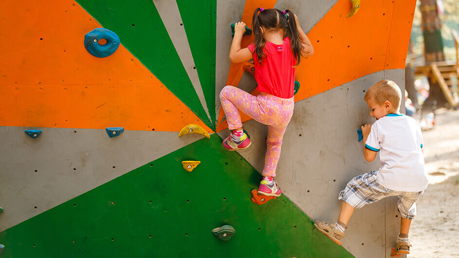 Ein Mädchen und ein Junge beim Klettern bzw. Bouldern auf einem Kinderspielplatz