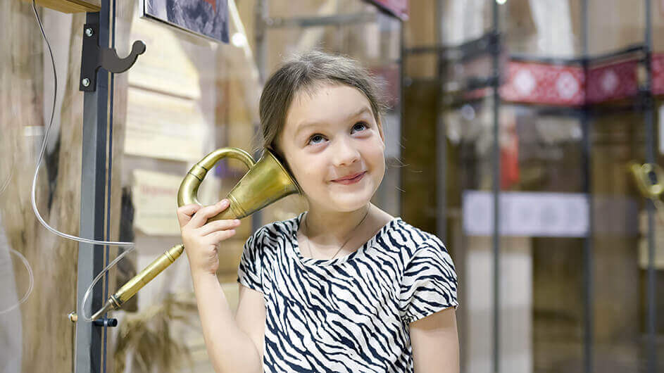 Ein Mädchen hört lächelnd etwas über ein altes Telefon/Kopfhörer an.
