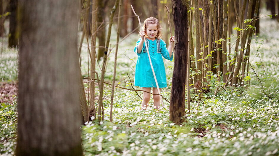 Ein Mädchen in einem blauen Kleid spielt im Wald mit Stöckern