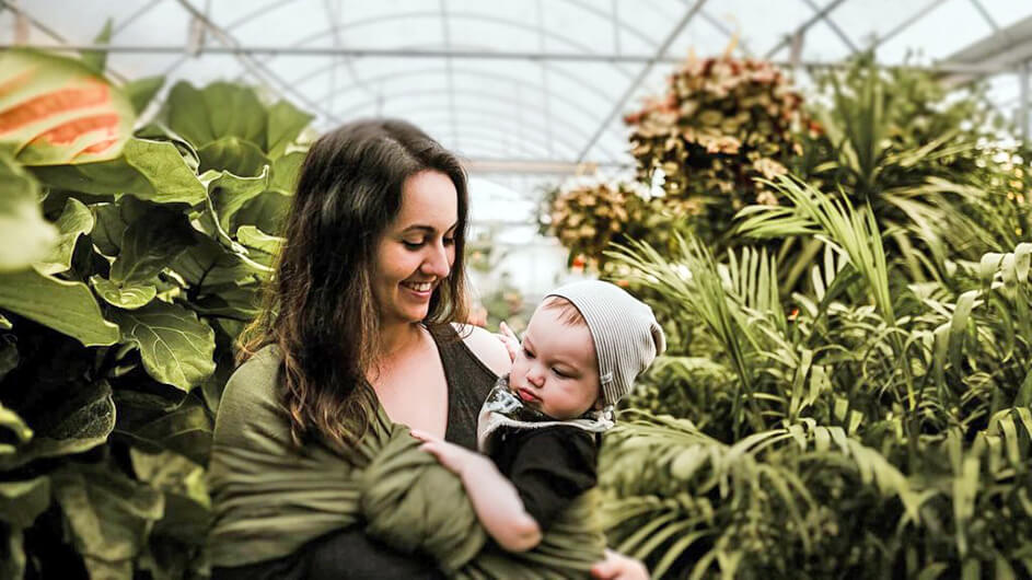 Eine lächelnde Mutter mit Baby auf dem Arm im Tropenhaus bzw. Gewächshaus