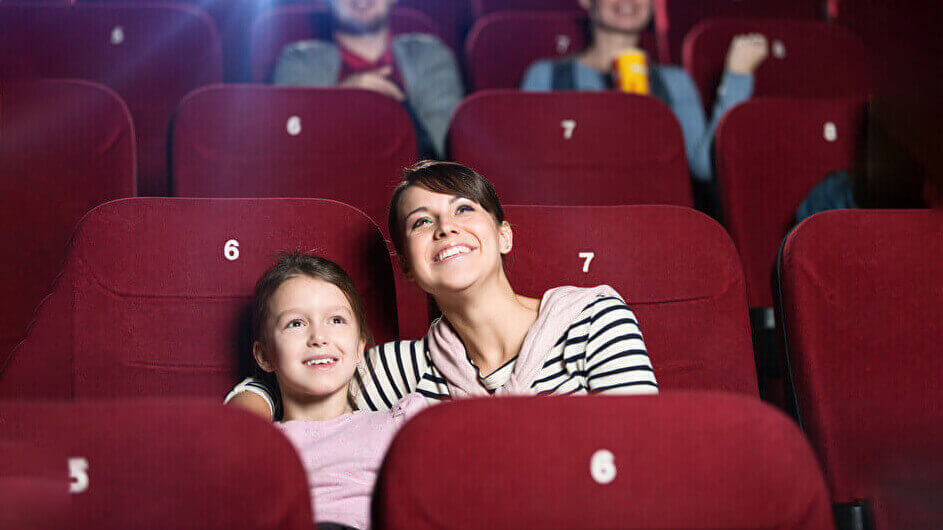 Mutter und Tochter im Kino beim Gucken eines Kinofilms: Beide lächeln