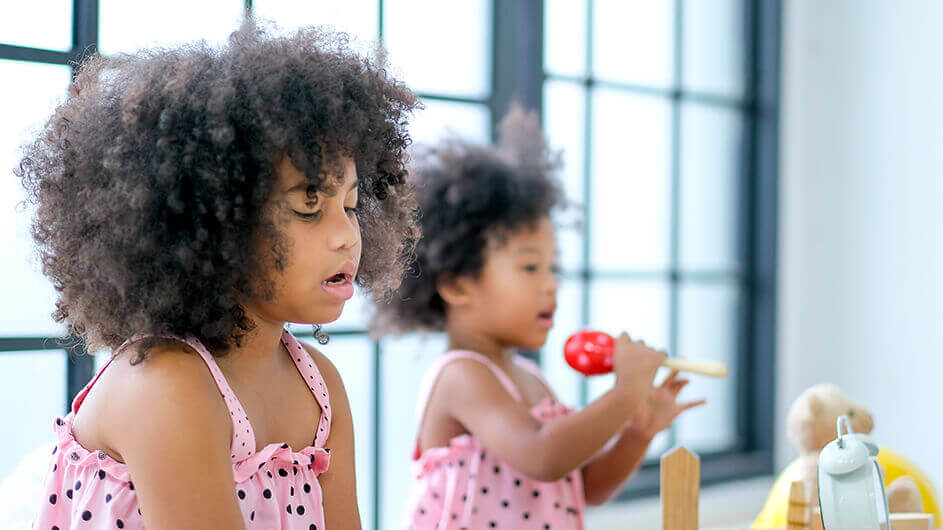 Zwei singende Mädchen: Beide sind ganz konzentriert. Ein Kind hält eine Rassel statt eines Mikrofons in der Hand.