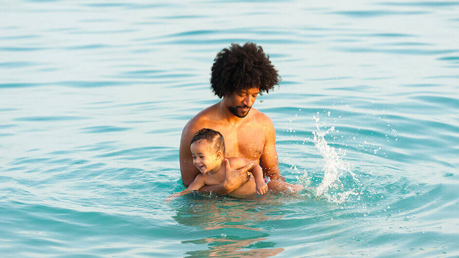 Ein Vater gewöhnt sein lächelndes Baby ans Wasser beim Babyschwimmen