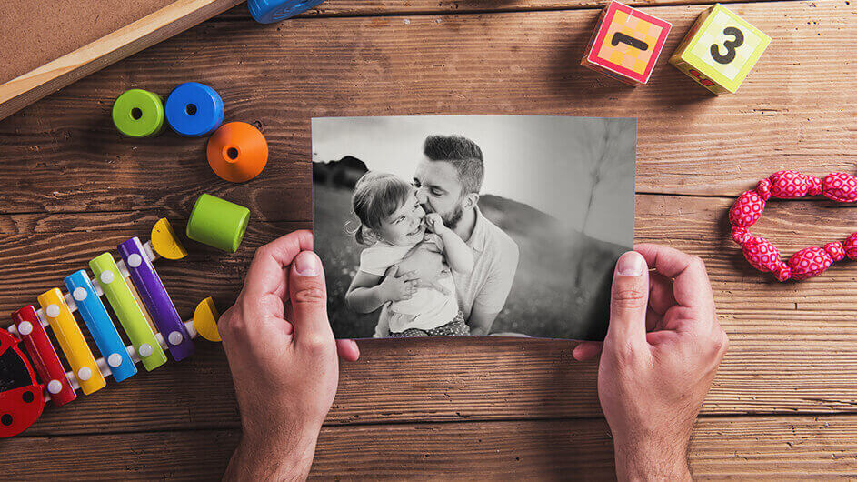 Ein vater hält im Kinderzimmer ein Foto von sich und seiner kleinen Tochter in den Händen. Auf dem Foto lachen beide