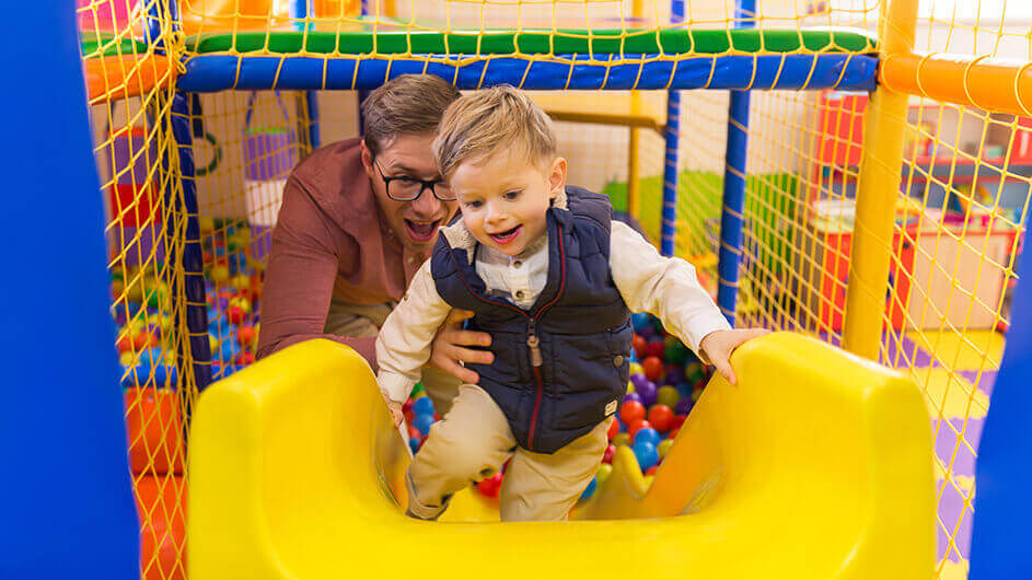 Ein Vater spielt mit seinem Sohn in einem Indoorspielplatz: Beide lachen.