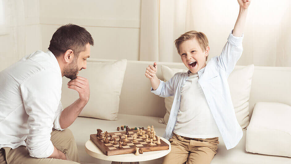 Ein Junge spielt gegen seinen Vater Schach und freut sich