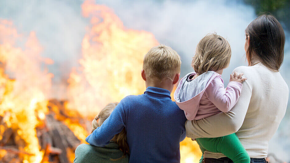 In der Rückansicht: Eine Familie vor einem Osterfeuer. Die Mutter hält ihre kleine Tochter auf dem Arm und zwei weitere Geschwister umarmen sich.