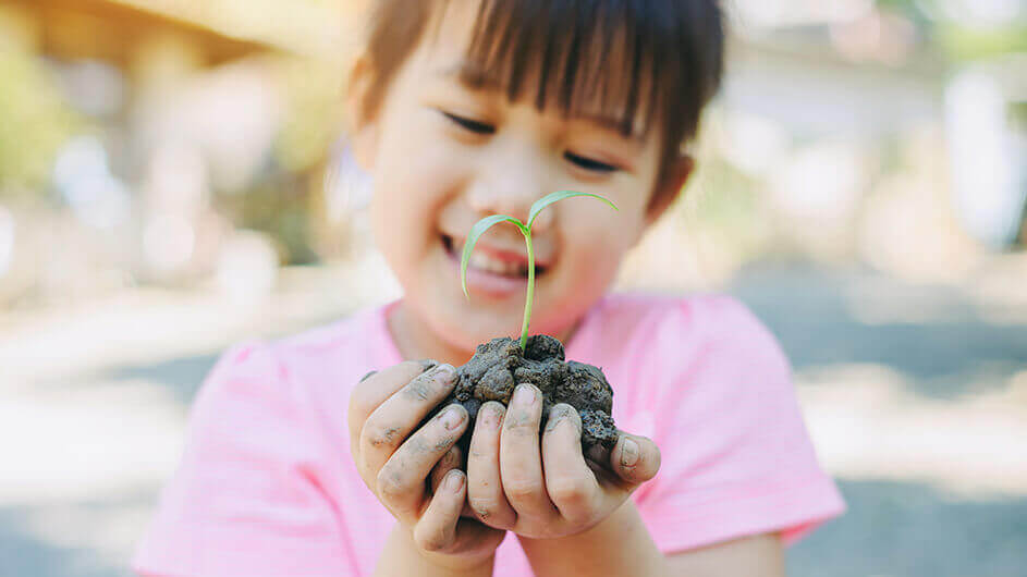 Ein Mädchen hält lächelnd Erde mit einem Pflanzenkeim in den Händen