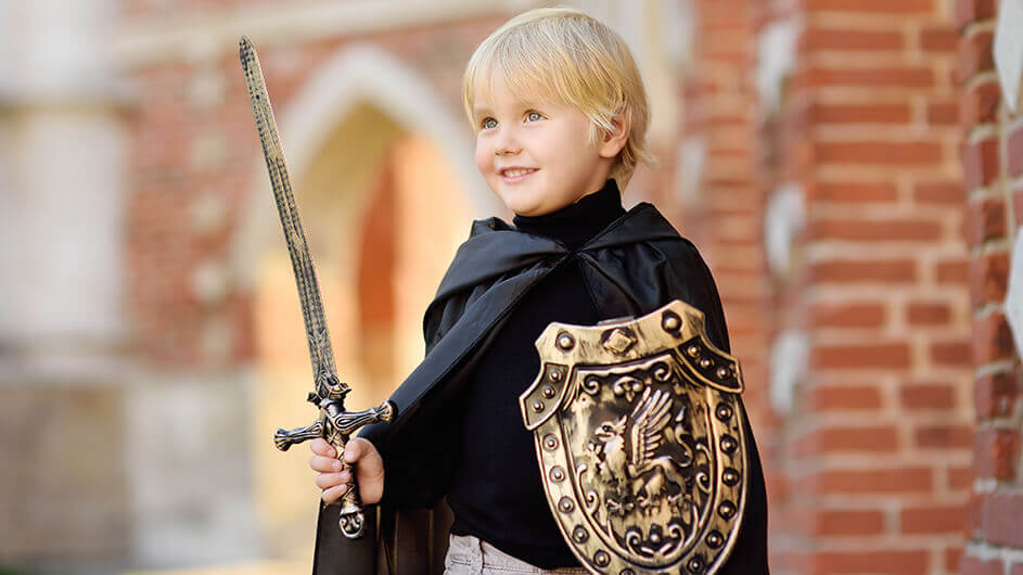 Ein Junge verkleidet als Ritter mit Umhang, Schild und Spielzeug-Schwert