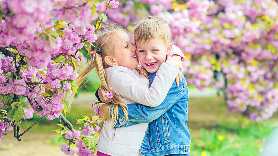 Zwei fröhlich lachende Kinder spielen zwischen Kirschblüten und umarmen sich