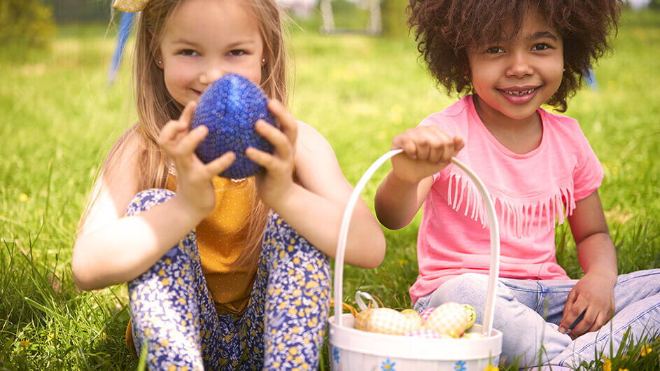 Zwei Kinder an Ostern mit Ostereiern: Beide sitzen lächelnd auf einer Wiese