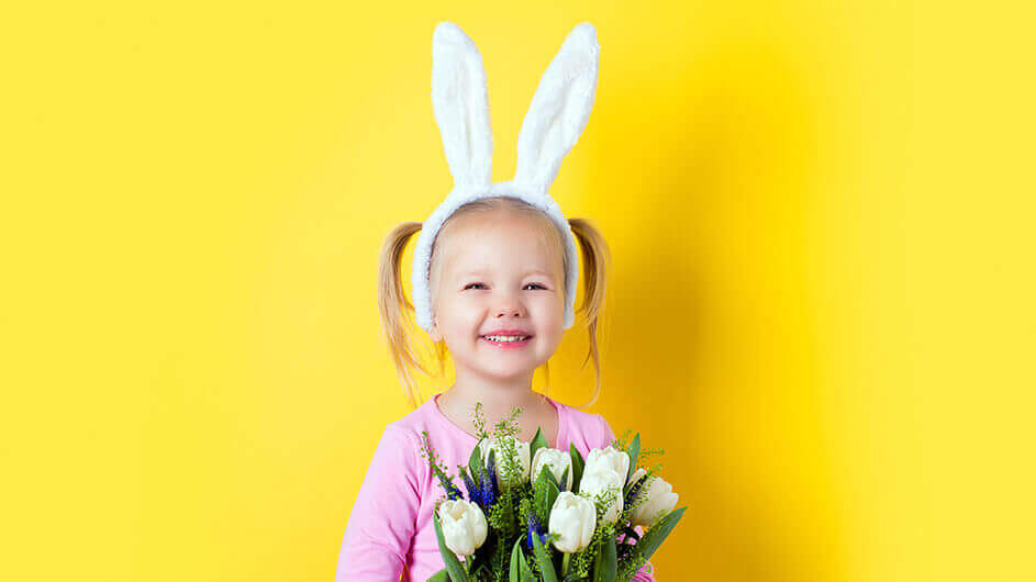 Ein lächelndes Mädchen mit Hasenohren und einem Blumenstrauß aus Frühlingsblumen