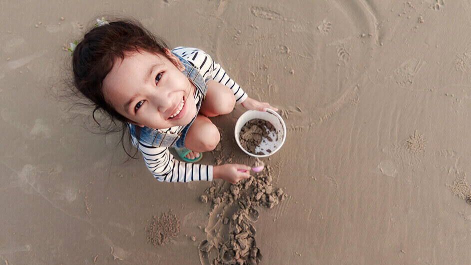 Ein Mädchen guckt lächelnd beim Spielen am Strand in die Kamera