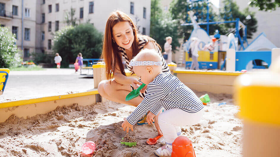 Mutter spielt mit kleinem Kind im Sandkasten auf Spielplatz