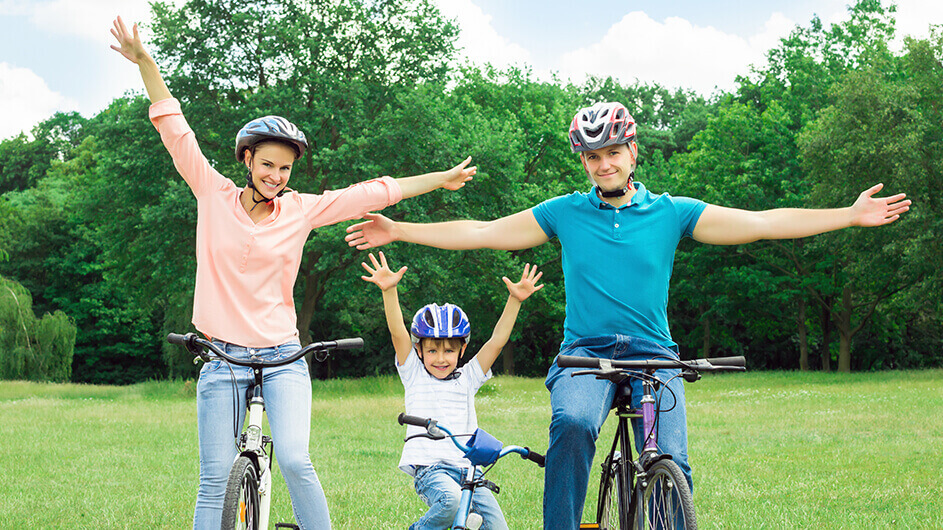 Eine fröhlich lächelnde Familie Helm tragend auf Fahrrädern. Sie strecken die Arme in die Luft.