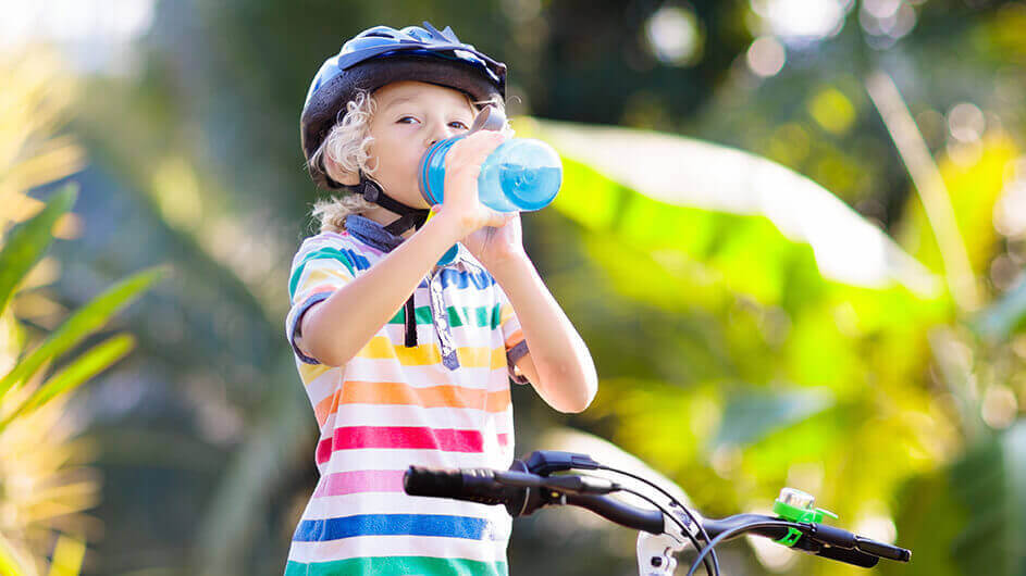 Ein Kind mit Fahrrad und Fahrradhelm trinkt aus einer Flasche.