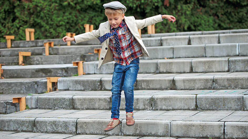 Ein kleiner, schick gekleideter Junge springt auf einer Treppe