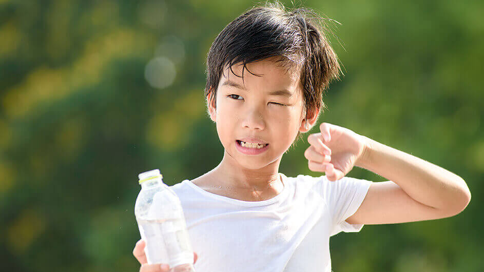 Schwitzender Junge im Sommer mit einer Wasserflasche.