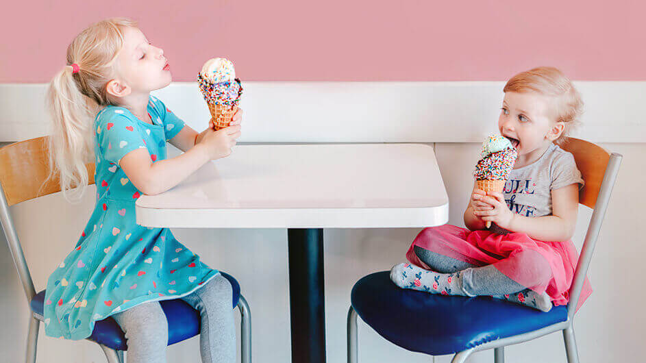 Zwei Kinder in einer Eisdiele beim Eisessen: Die Eiskugeln sind in Waffeln und mit bunten Zuckerstreuseln bestreut