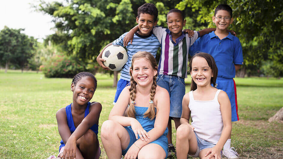 Sechs lächelnde Kinder mit einem Fußball im Park