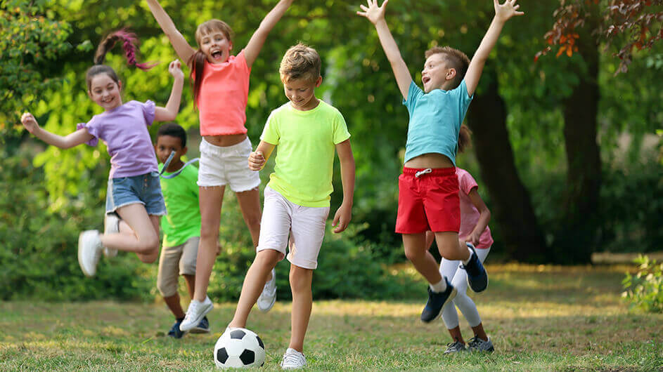 Jubelnde Kinder beim Fußballspielen im grünen Park