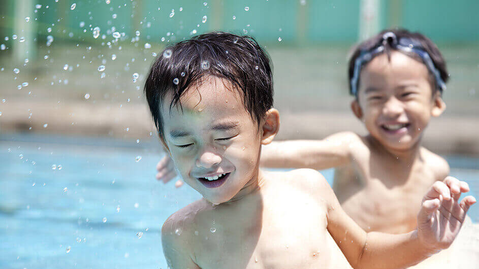 Zwei lachende Kinder beim Planschen und sich mit Wasser bespritzen im Freibad.