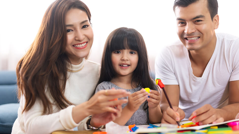 Eltern spielen mit ihrer Tochter mit bunter Knete. Alle drei lächeln.