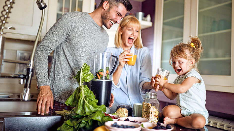 Frühstuecken mit Kindern; Vater, Mutter, Kind mit Müsli, Blaubeeren, Gemüse für Smoothie und Orangensaft